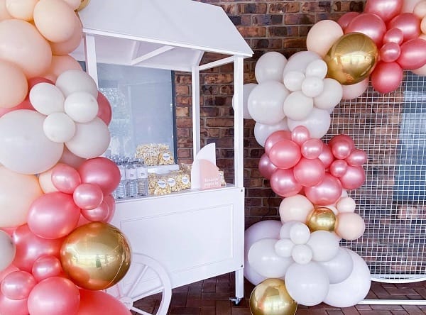 Baby shower decorations with balloons and a quaint pop corn cart.