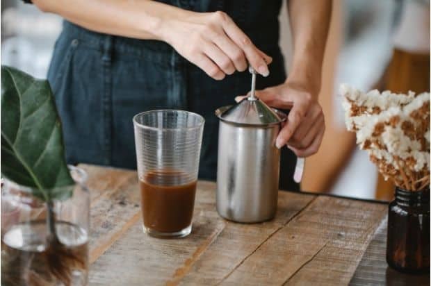 Barista pumping the plunger on a stainless steel French press to make cold foam