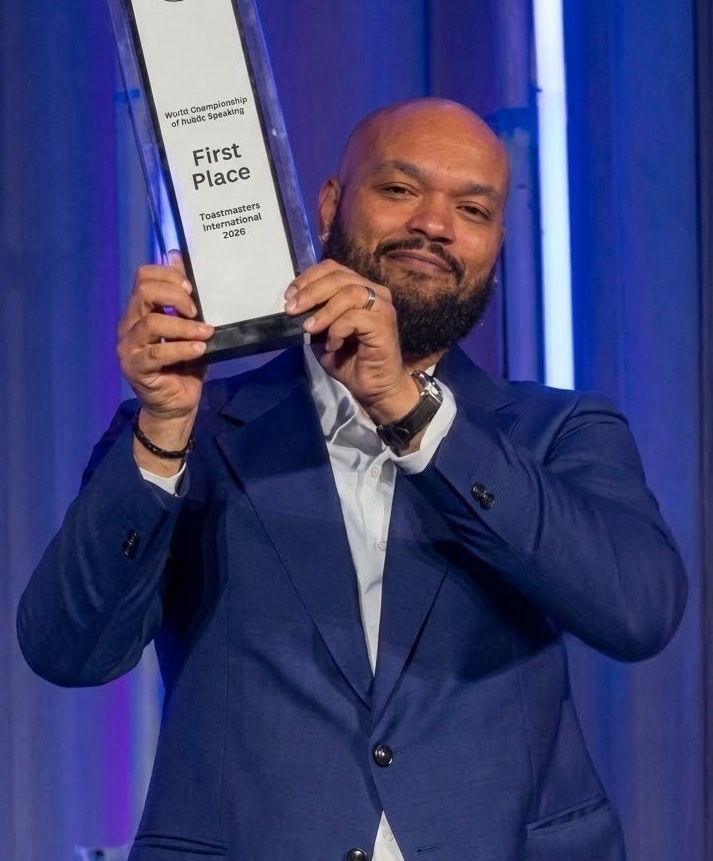 Dirceu da Silva holding his trophy after winning the 2026 World Championship of Public Speaking, coached by Pres Vasilev, 2013 World Champion of Public Speaking.