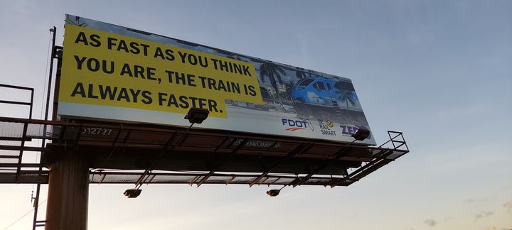 Billboard reading As fast as you think you are, the train is always faster, photographed from below against a blue sky.