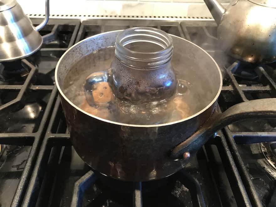 Mason jar full of coffee beans simmering in a pot of water