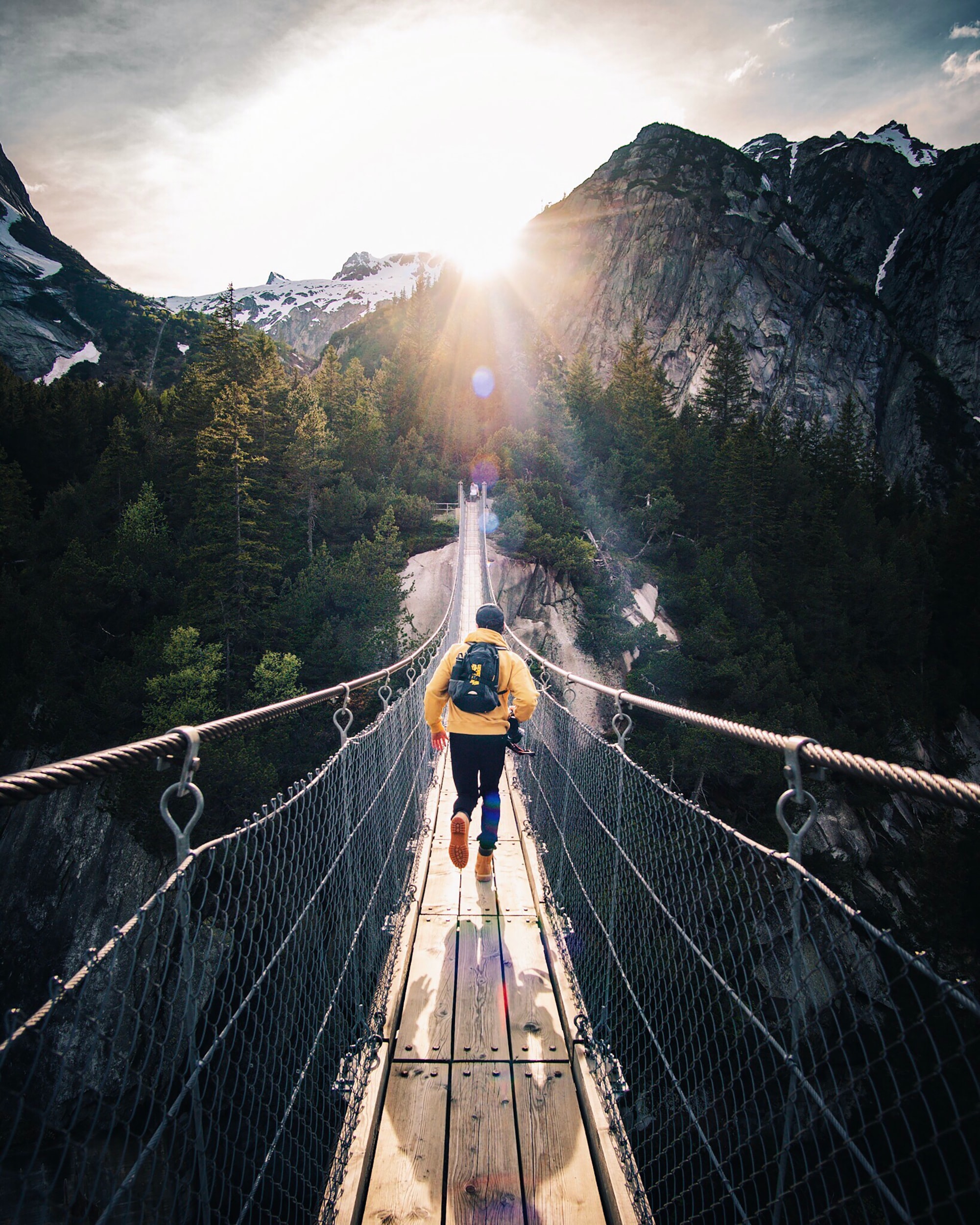 Person läuft über eine Hängebrücke in den Bergen — Symbol für den Übergang in eine neue, vernetzte Arbeitswelt.