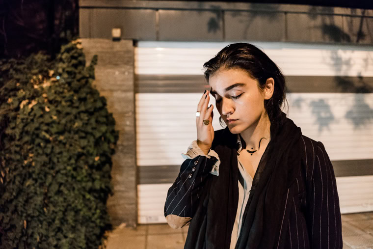 Iranian female singer Meshkat standing on the street at night, contemplating.