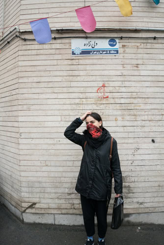 Iranian singer Meshkat hiding behind her scarf and holding her head in a public alley.