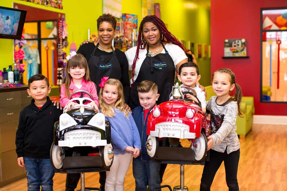 stylists at Pigtails & Crewcuts kid's haircut franchise with kids in front