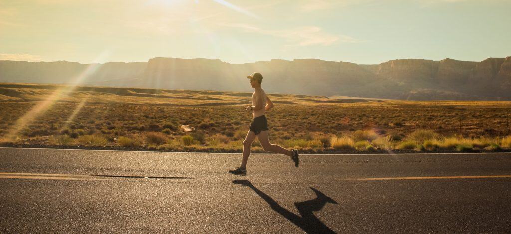 A runner running on a road across the desert in North America with the sun behind him