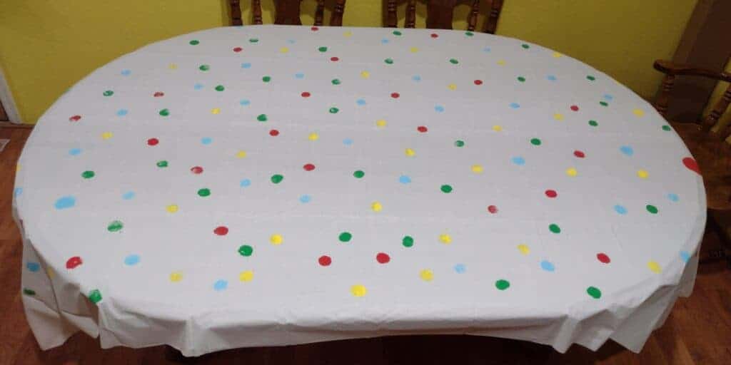Picture of a polka dot tablecloth. It is white with red, green, yellow, and blue polka dots painted on