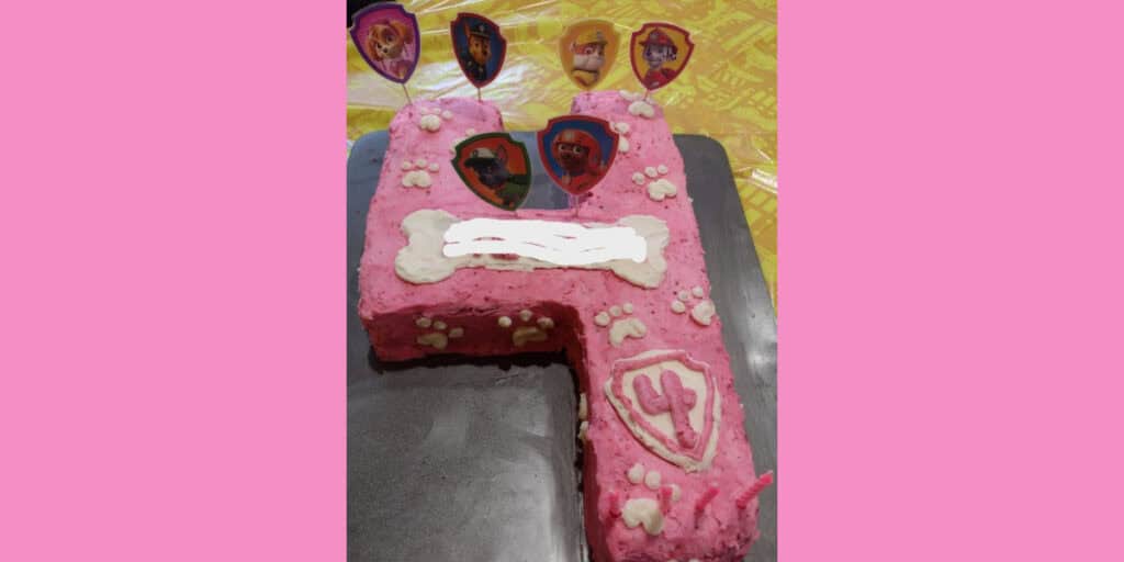 Picture of a pink Paw Patrol cake. A dog bone, paw prints, and a badge with a pink number 4 are all on the cake in white frosting