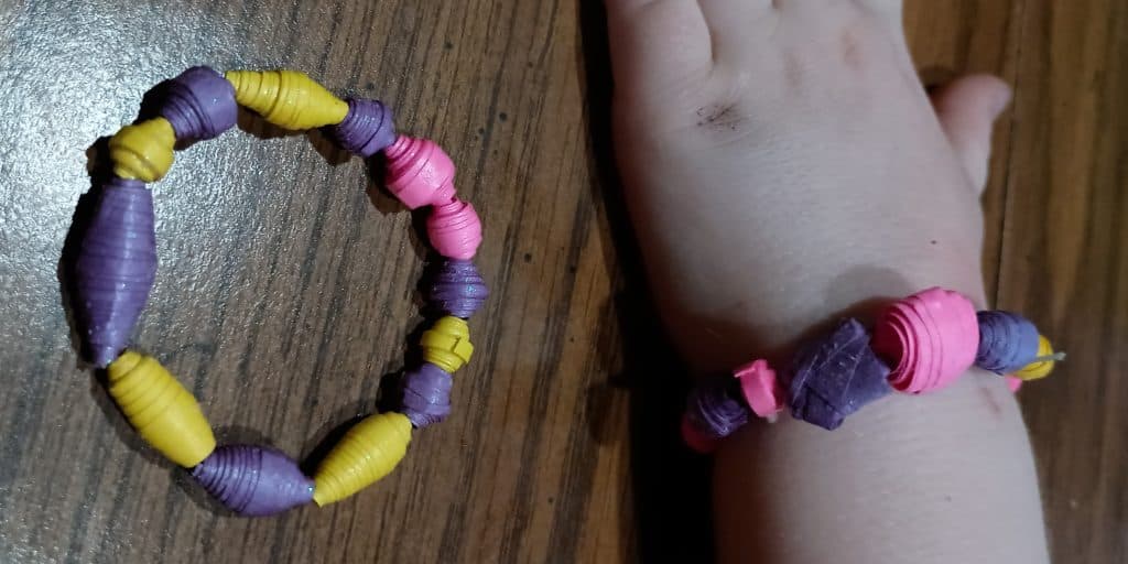 Picture of two glow in the dark bracelets made from paper beads. One is just sitting on the table and one is on the wrist of a preschooler