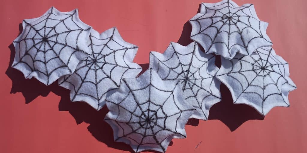A pile of spiderweb felt toys. They are made of two pieces of white felt with spiderwebs drawn on them and then stuffed.