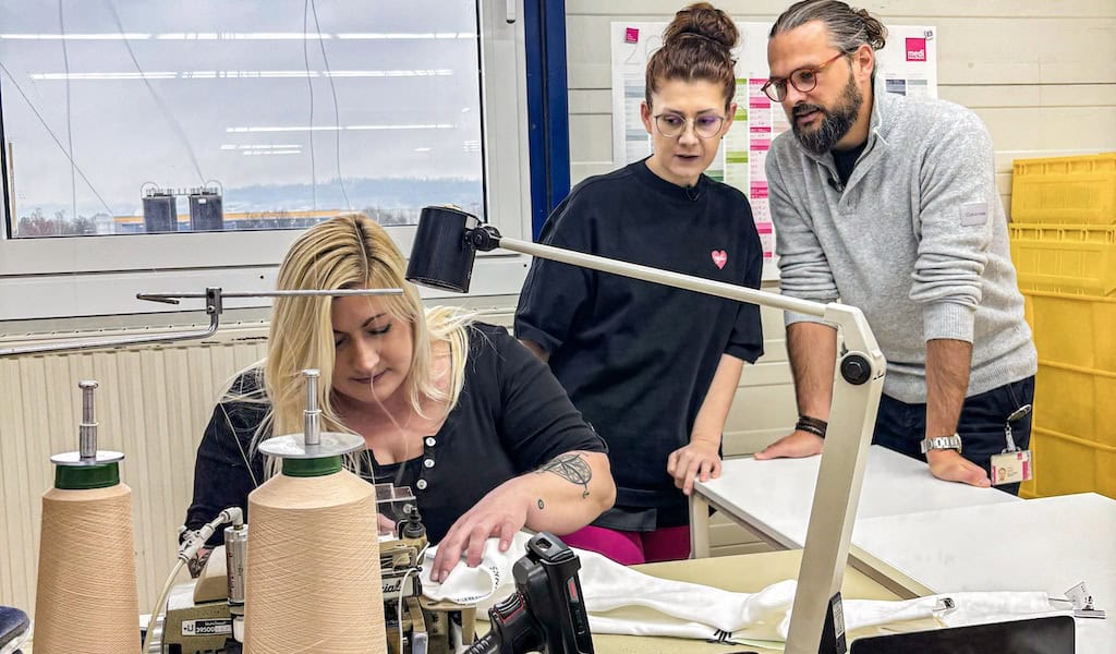 Die bekannte Buchautorin, TikTokerin und medi Testimonial Jana Crämer erhielt bei einer Werksführung Einblicke in die Produktion eines flachgestrickten medizinischen Kompressionsstrumpfes von medi. Im Bild (v. l. n. r.): Julia Schretzmeier (Näherin Konfektion bei medi), Lip-Lymphödem-Patientin Jana Crämer und Philipp Schatz (Geschäftsführung bei medi). (Bild: © www.medi.de)