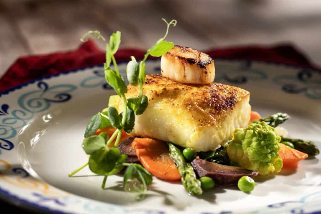 Disney Treasure Plaza de Coco Pan-seared adobo Spiced Sea Bass with seared scallops, rainbow carrots, spinach, romanesco, peas and chimichurri sauce