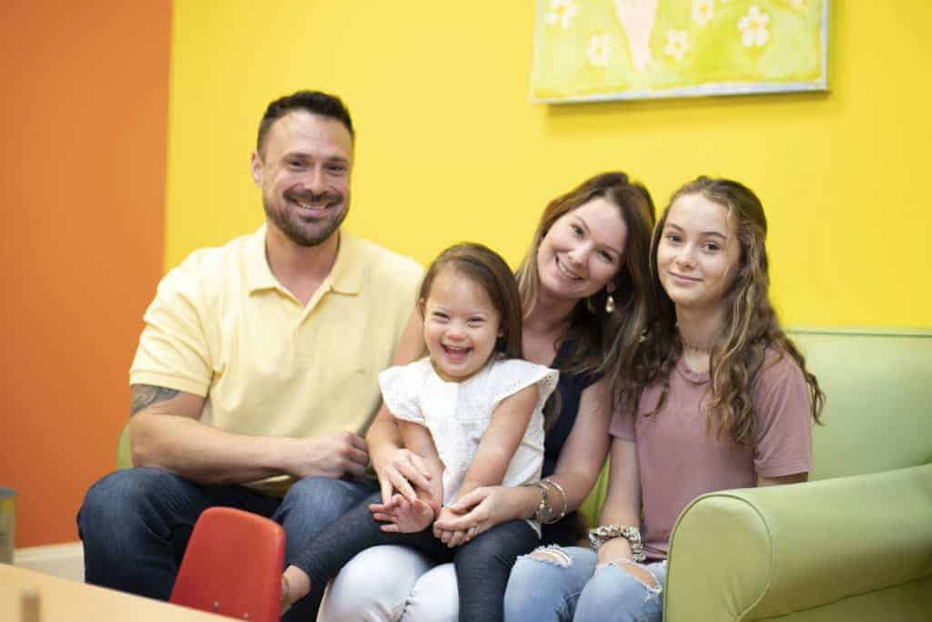 happy family, mom, dad and two daughters sitting on couch in pigtails & crewcuts franchise