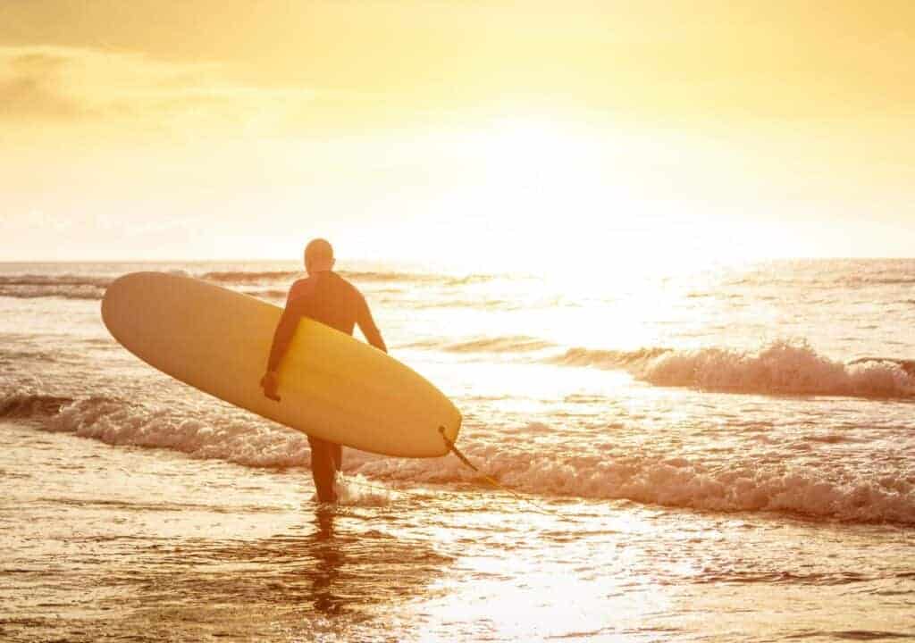 Surfer walking through the surf on a beach in Portugal at sunset