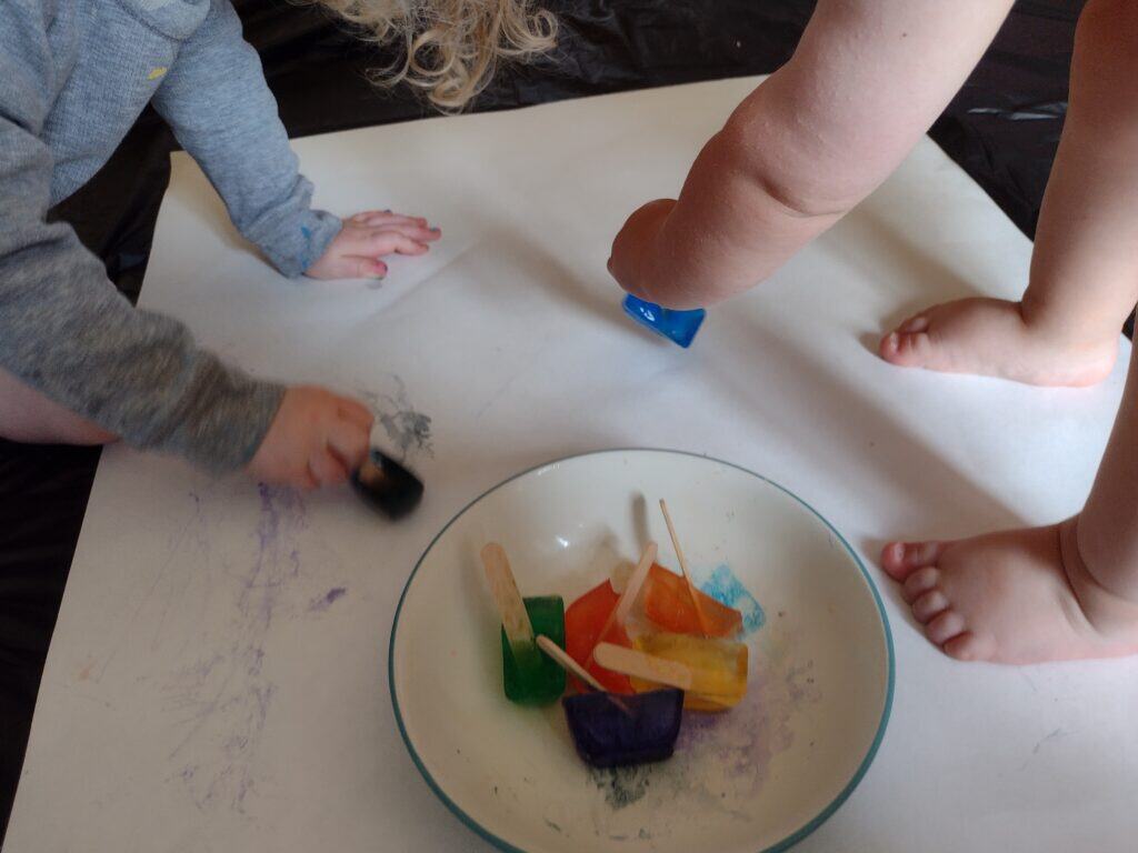 Picture of a toddler and a preschooler painting with ice on a large piece of paper