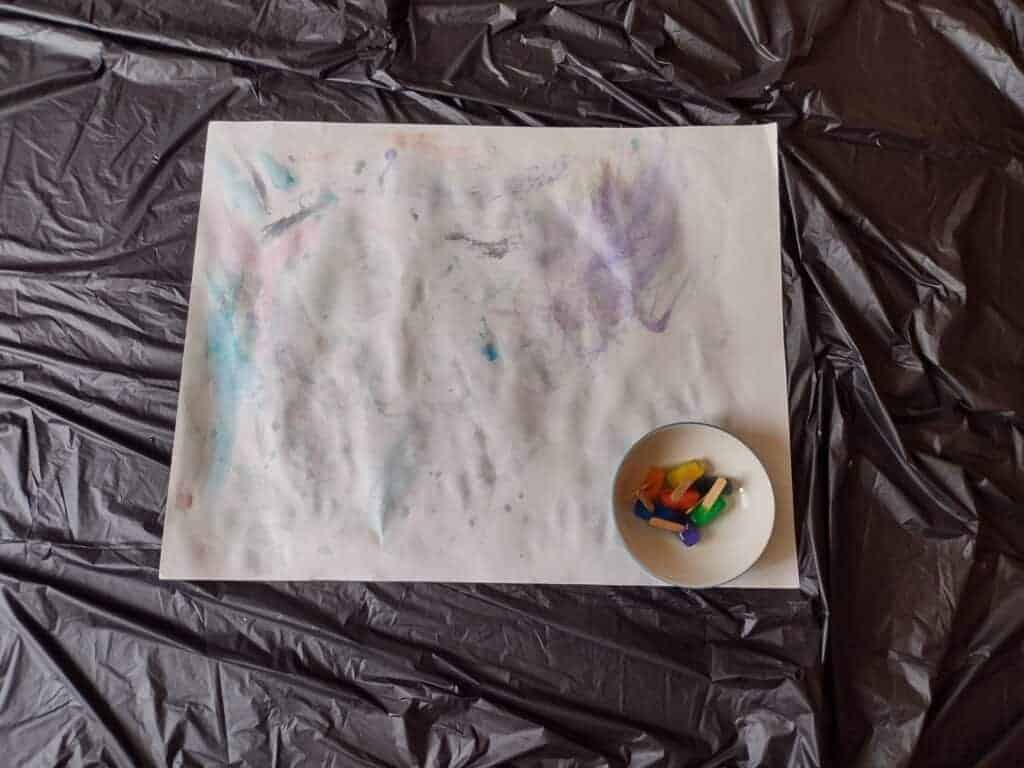 Picture of piece of paper after painting with ice with not enough food coloring. Colored ice cube sticks are in a bowl in the corner