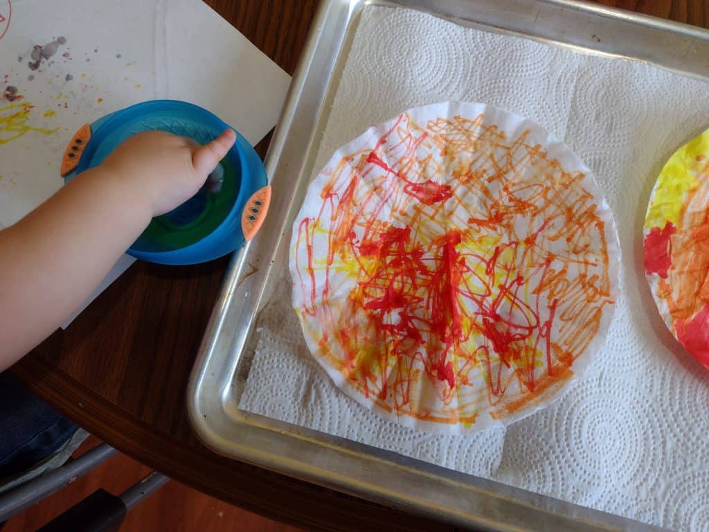 Picture of a toddler dipping his hand in a bowl full of water next to a colored coffee filter