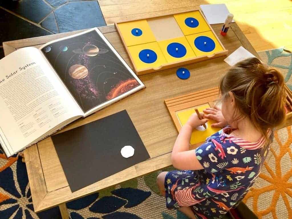 Montessori First Great Lesson Follow-up work: child tracing Geometry Cabinet Circles Drawer and Planetarium book open to The Solar System