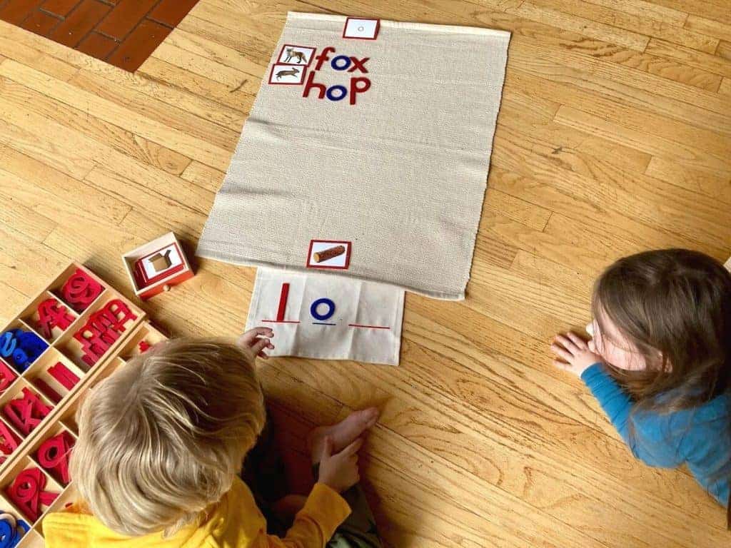two children sitting on the floor next to red and blue letters and a drawer with image cards