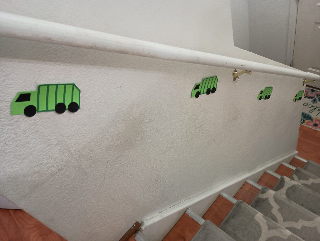 Picture of little paper garbage trucks on the wall leading up a flight of stairs
