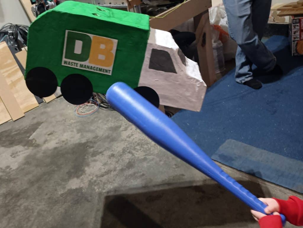 Picture of a three year old swinging a bat at a trash truck pinata at a garbage truck birthday party