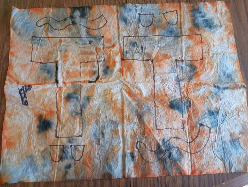 Picture of an orange and black tie dyed piece of tissue paper with a T, a tiger tail, and tiger ears drawn on it