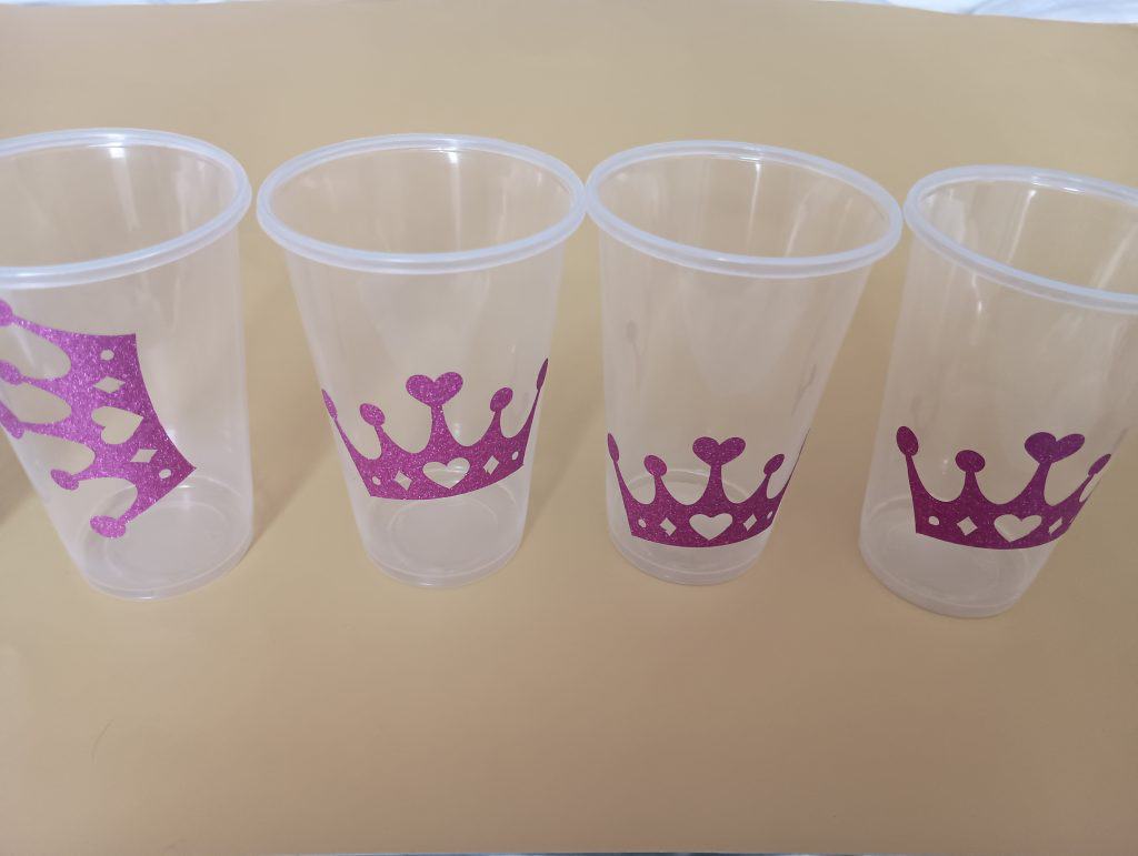 Picture of clear plastic cups with pink glittery vinyl tiaras on them