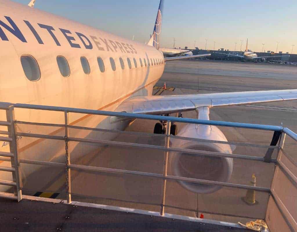 The back end of a United Airlines plane as seen from the steps to the door while boarding at sunset.