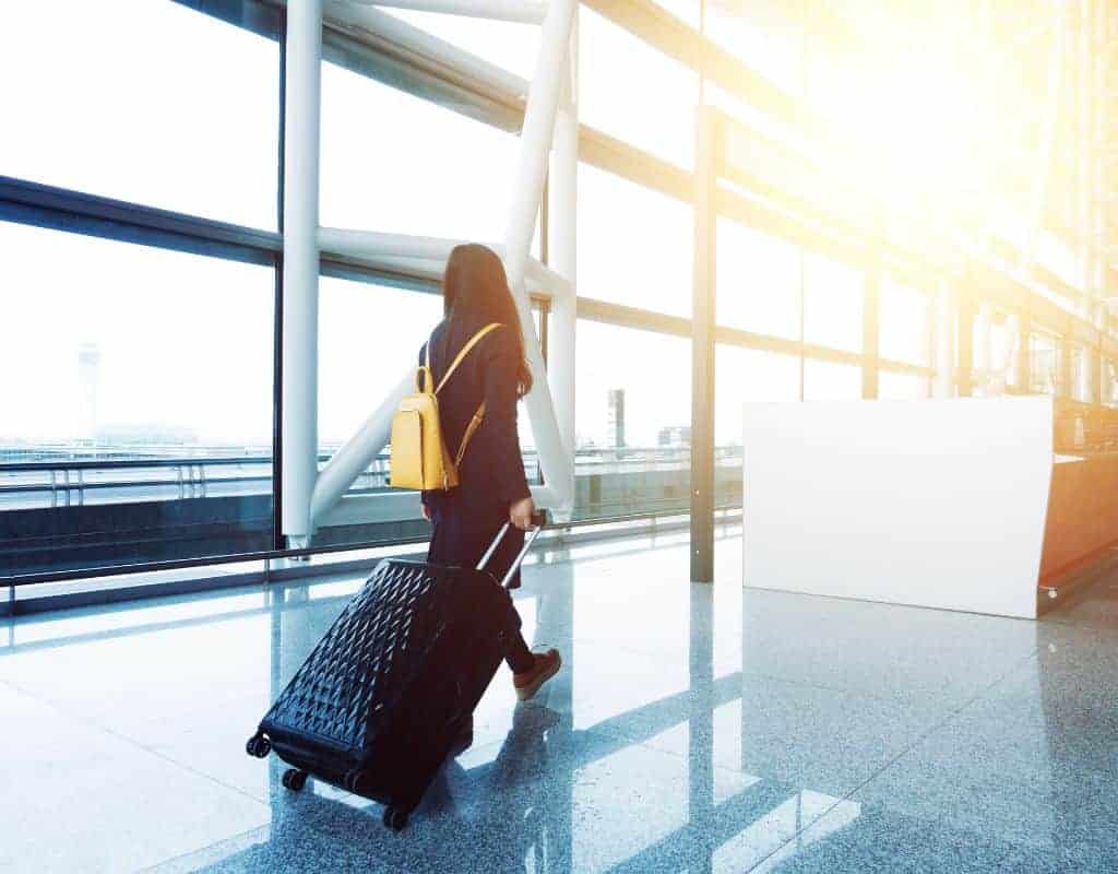 Woman dragging her suitcase up to a counter in the airport with the control tower and tarmac seen behind her out the window.