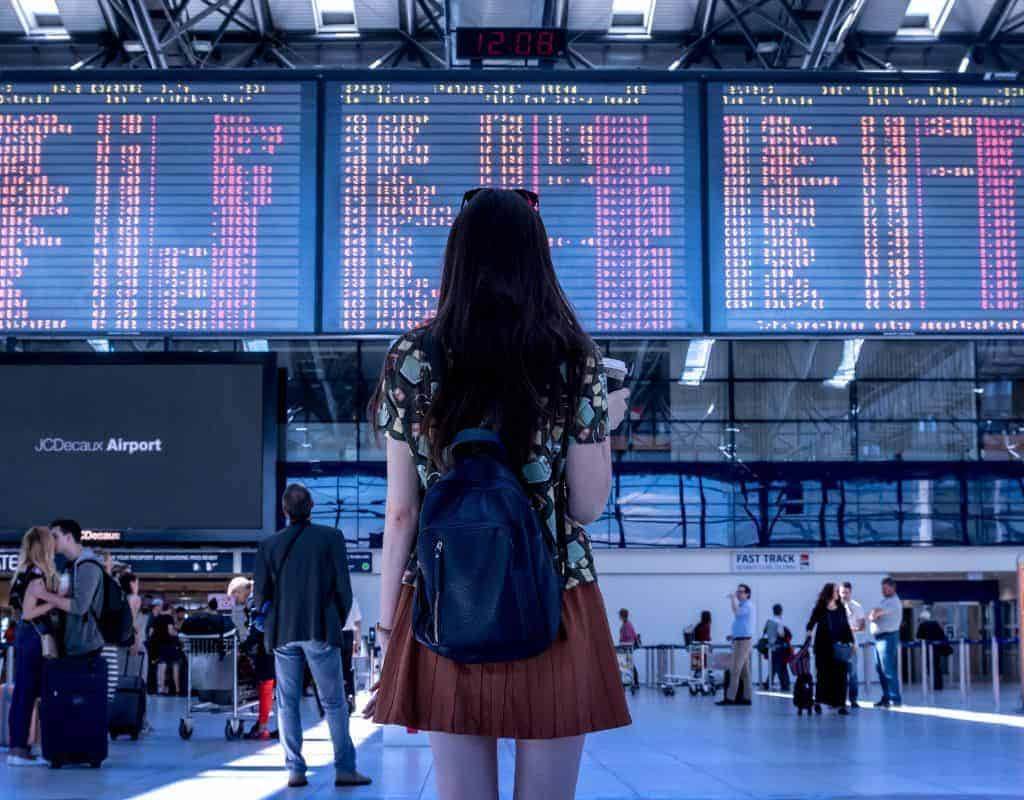 Girl looking at the flight information screens in Lisbon's busy check in area. If you know which gate you are going to this can reduce your Lisbon Airport security wait time.