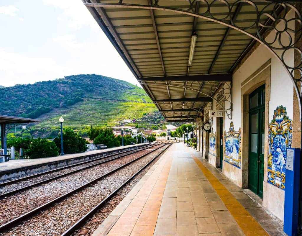 The Peso da Regua scenic train station platform with colorful tile murals, nestled against a backdrop of lush green hills and terraced vineyards, illustrating the route from Porto to Douro Valley by Train.