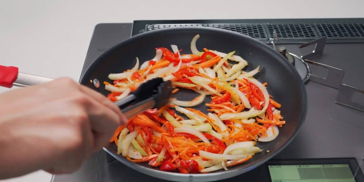 Stir-frying carrots, celery, onions and bell peppers in a frying pan.