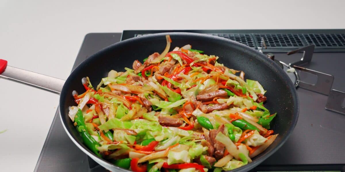 Chop Suey with pork, cabbage, carrots, peppers, snap peas, celery and onions in a frying pan.
