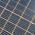Vista aérea de un parque fotovoltaico español de gran escala con miles de paneles solares azules en alineación geométrica, capturada desde 150 metros de altura en luz cenital