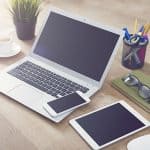 A desk with a laptop, mobile phone and tablet, along with other office equipment