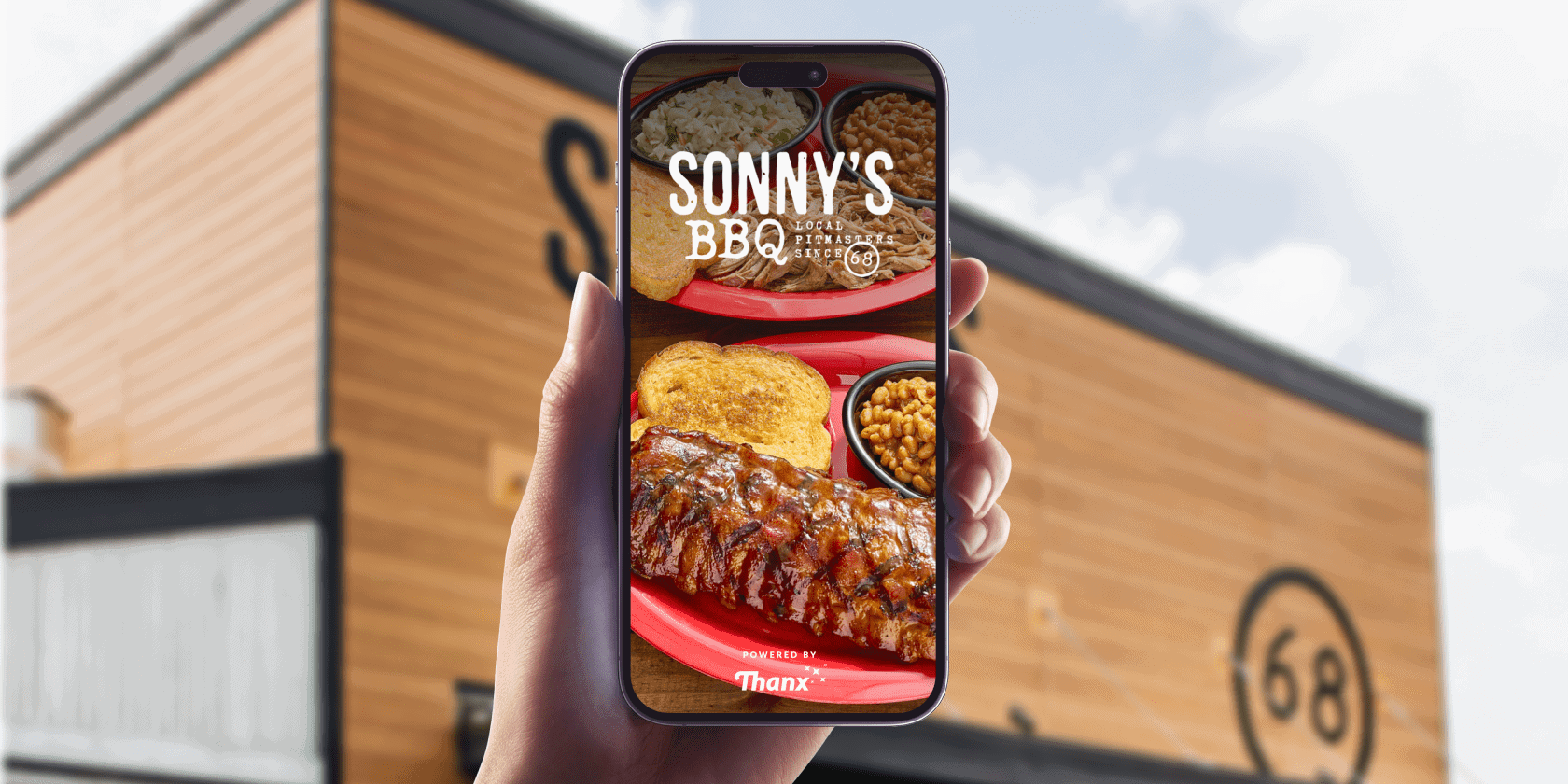 Hand holding a smartphone in front of a Sonny’s BBQ restaurant. The phone screen displays a plate of barbecue food with ribs, toast, beans, and coleslaw, along with the Sonny’s BBQ logo and the text “Powered by Thanx.