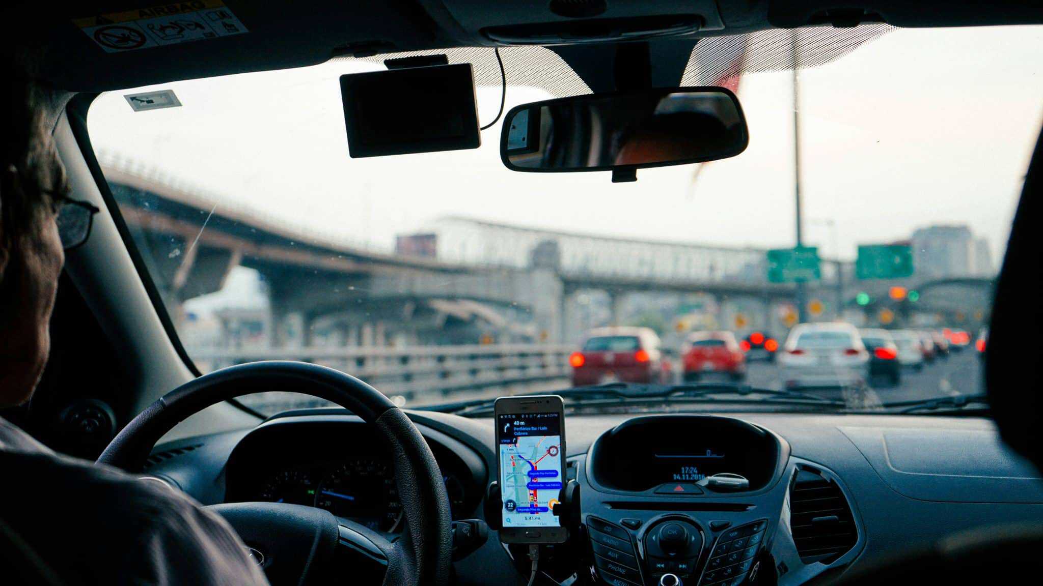 rideshare driver in nyc wth maps on his phone, pov from the backseat looking out