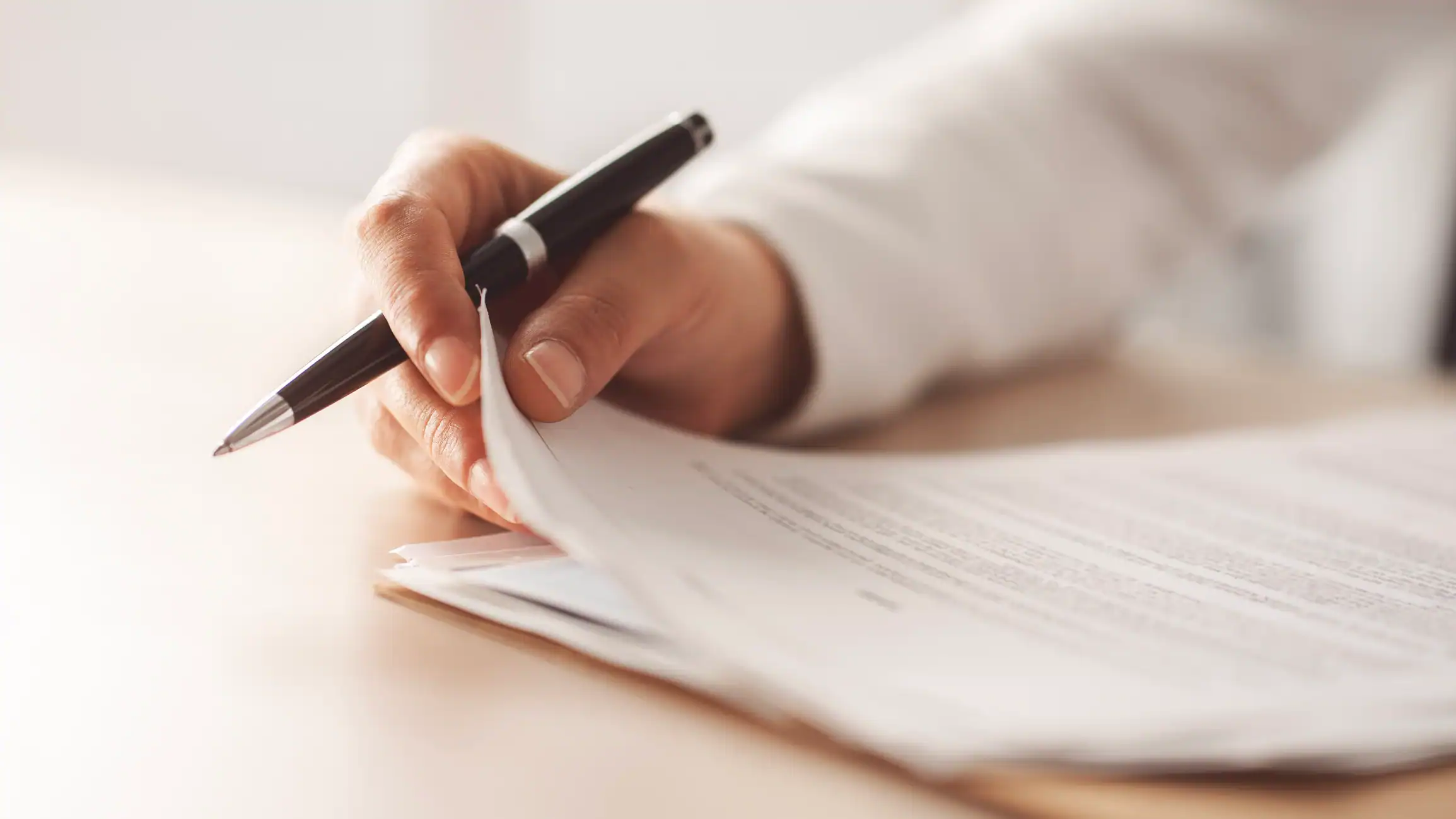 A hand holding a pen and some paper on a table