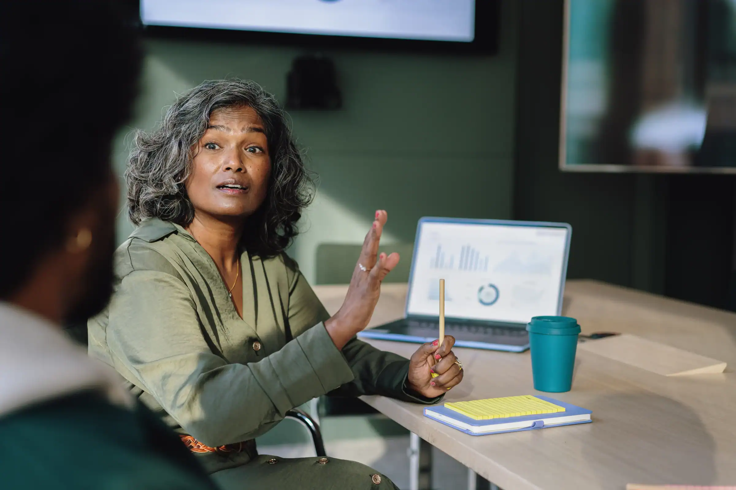 Colleagues in business performance meeting in office. Female colleague looks back and talks to colleague. Shot over the shoulder of colleague. Strategy documents show on laptop screen