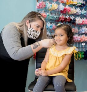 Pigtails & Crewcuts stylist piercing a customer's ears