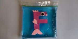 Picture of a foam F is for fish craft made by a preschooler floating in a food coloring blue water filled plastic bag
