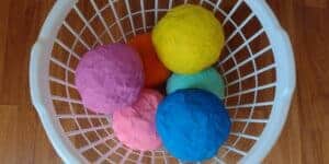 Picture of 6 pinata balls in a laundry basket. There is an orange, yellow, green, blue, pink, and purple one