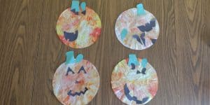 Picture of four easy pumpkin crafts for kids. There are made from tied dyed coffee filters with construction paper jack o'lantern faces glued on