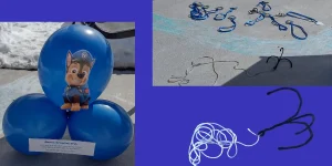 Picture of a Chase Paw Patrol themed party game. On the left are three blue balloons with directions and a picture of Chase taped to them. On the right is a picture of the game itself with a chalk river in the middle of a pipe cleaner grappling hook and pup badges. A cut out picture of the grappling hook is at the bottom