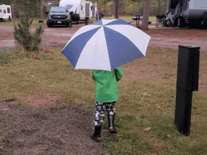 kid with umbrella, rain jacket and rain boots, camping in the rain