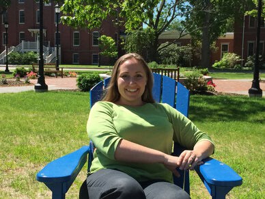 Courtney Mejia, Student Service Advisor for our online science prerequisites, sits in a blue chair on the UNE Portland campus lawn