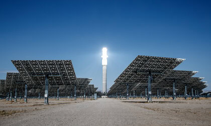 Desert solar thermal plant with hundreds of heliostat mirrors surrounding a tall central receiver tower.