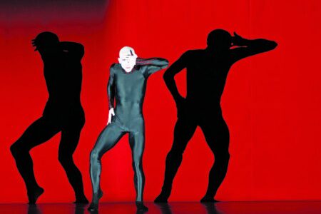 Der schwarte Kautschukmann und seine Schatten, die sich im roten Vorhang verselbständigen.