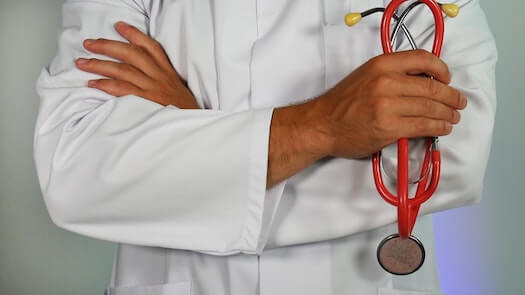 Torso of a doctor with his arms crossed and holding a folded stethoscope