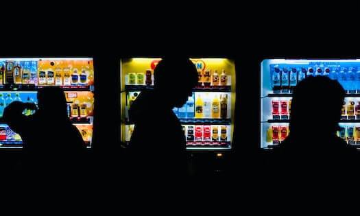 Silhouettes Passing by Lit Vending Machines